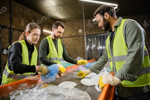 Preview: Multiethnic workers in protective vests and gloves taking trash from conveyor while working together