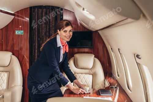 Preview: smiling flight attendant putting cup of coffee on table in private plane