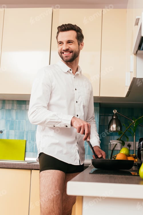 Preview: Selective focus of smiling man in shirt and panties cooking breakfast in kitchen