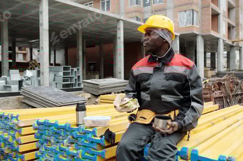 Preview: Restful mature builder with snack and cup of tea sitting on stack of materials