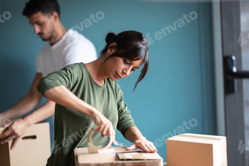 Preview: Attractive young couple packing boxes to move to new flat in living room at home.