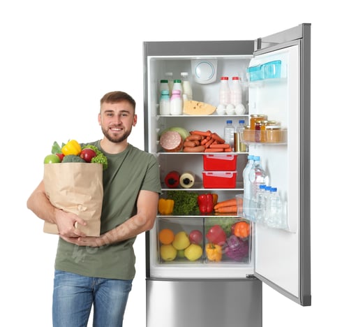 Preview: Young man with bag of groceries near open refrigerator on white background