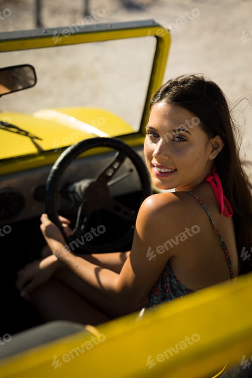 Preview: Happy caucasian woman sitting on beach buggy by the sea looking to camera
