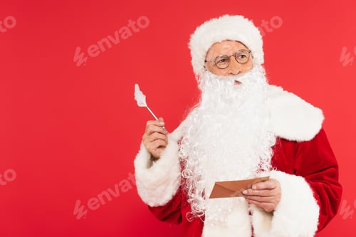 Preview: Pensive santa claus holding pen and envelope isolated on red