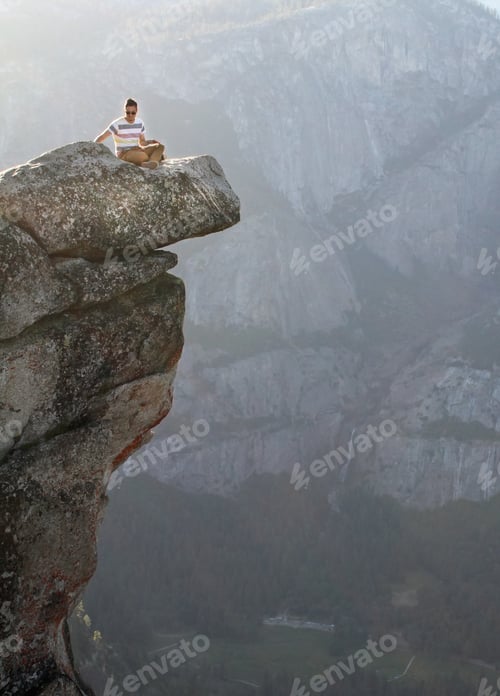 Preview: Vertical shot of a man sitting on a stone in front of the mountains in Yosemite National Park
