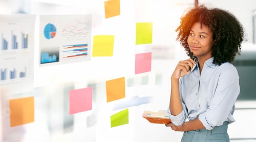 Preview: Young businesswoman using sticky notes in glass wall to writing strategy business plan success
