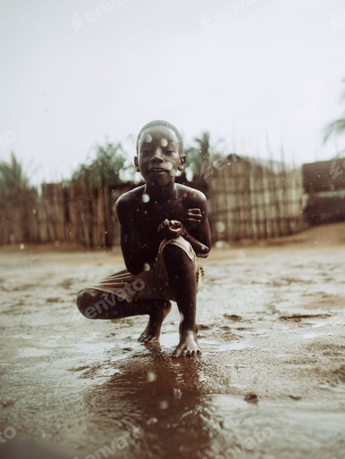 Preview: Young Mozambican boy standing in a muddy field in the rain.