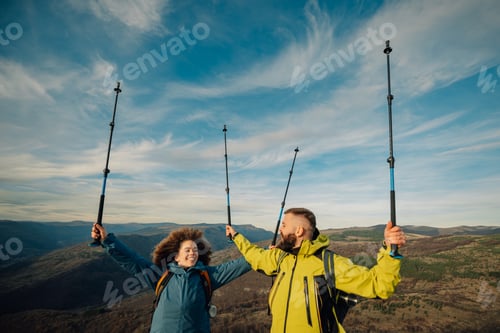 Preview: Hikers celebrating reaching mountain top with trekking poles raised high