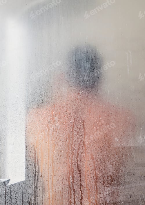 Preview: Silhouette of adult caucasian man in shower cabin and showering and wet glass background