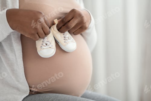 Preview: Unrecognizable Black Pregnant Lady Holding Little Baby Shoes Near Her Tummy