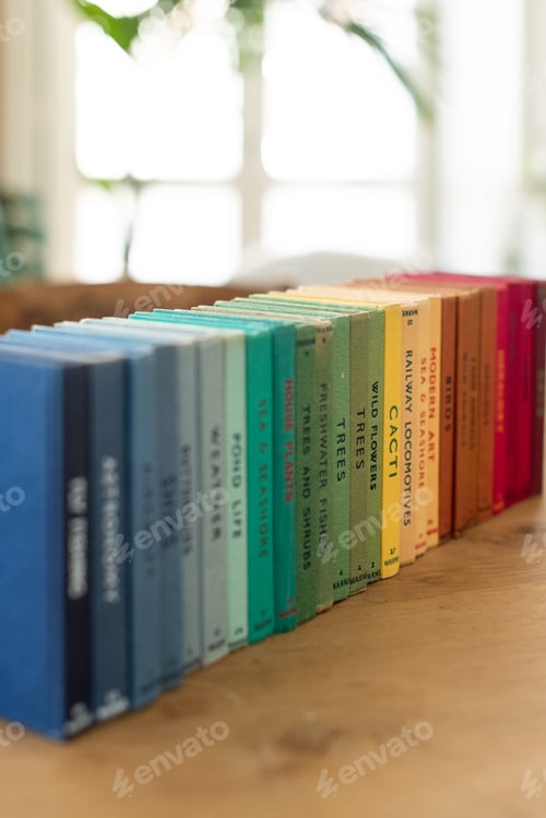 Preview: Vertical shot of stacked colorful books on different fields on the table with a blurry background
