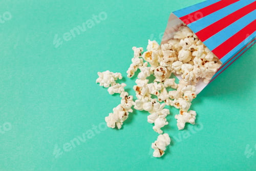 Preview: Popcorn spills from a striped box on a bright background during snack time