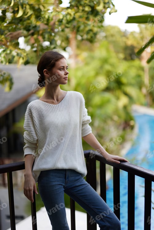 Preview: Smiling Woman Enjoying Tropical Vacation A happy young woman stands on a trendy balcony, overlooking