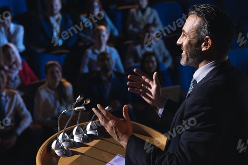 Preview: Side view of Caucasian businessman standing and giving presentation in the auditorium