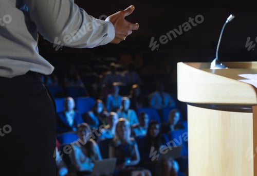 Preview: Rear view of businessman giving presentation in front of audience in auditorium