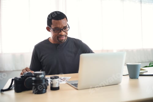 Vista previa: Apuesto fotógrafo africano cargando archivos en el ordenador portátil en su lugar de trabajo
