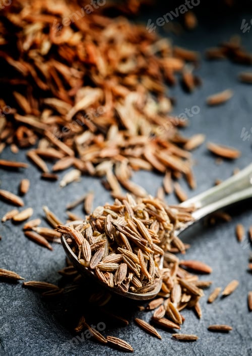 Preview: Zira or cumin in a metal spoon on a dark background, close-up