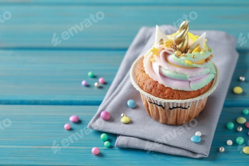 Preview: Cute sweet unicorn cupcake and festive decor on light blue wooden table, space for text