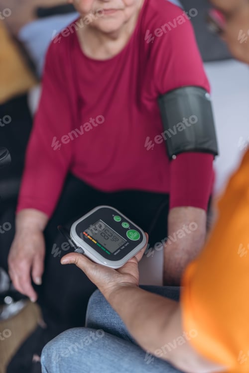 Preview: An elderly woman sits on a bed and has her blood pressure taken by a female volunteer