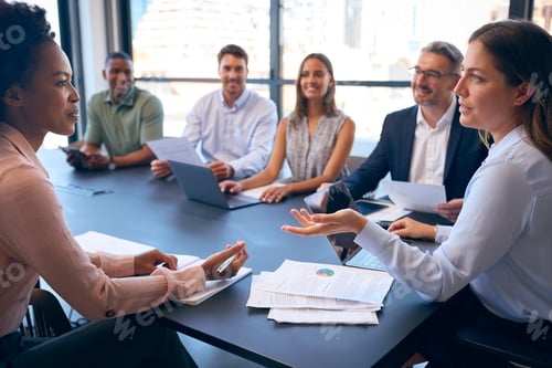 Preview: Multi-Cultural Business Team Meeting Around Office Boardroom Table With Laptops Discussing Documents