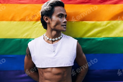 Preview: Portrait of a handsome guy looking away while standing against rainbow LGBT flag