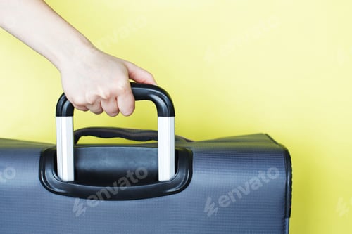 Preview: hand holding a suitcase isolated on a yellow background. Air flight journey concept.