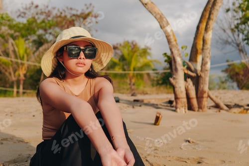 Preview: Calm young Asian woman sitting and posing in the beach with a dreamy expression.
