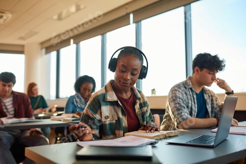 Preview: Black female student with headphones learning at college classroom.