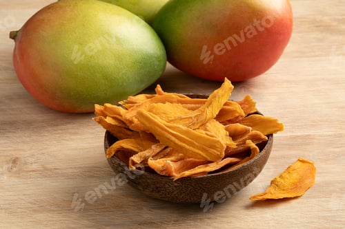 Preview: Bowl with dried mango chips close up and fresh mango at the background