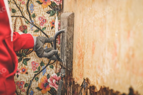 Preview: Hands of a young caucasian guy removes retro wallpaper using a steamer machine in an old house.