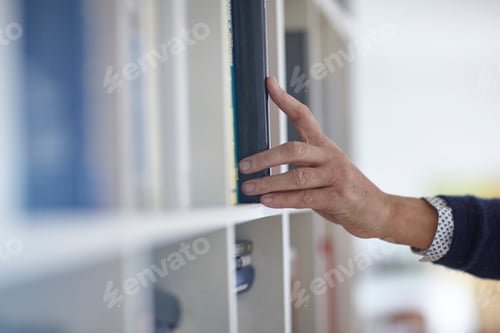 Preview: Hand of mature woman selecting book from bookshelves