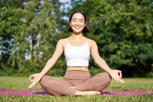 Preview: Sporty woman meditating on fresh air, sitting on fitness mat and practice yoga, smiling pleased