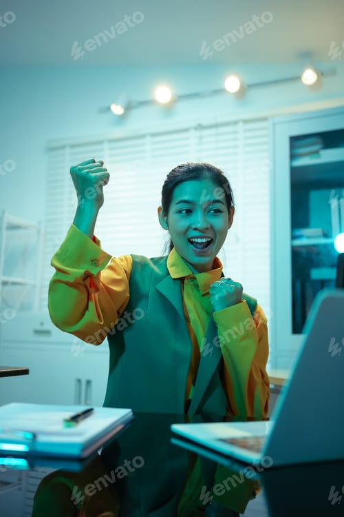 Preview: Asian businesswoman celebrating success at her desk, delighted after achieving business goals
