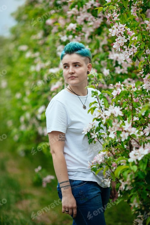 Preview: A young girl with bright hair stands in a field among flowering trees.