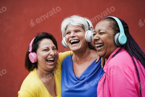 Preview: Happy mature female friends having fun together while listeing music with wireless headphone