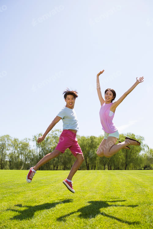 Preview: Cheerful young man and young woman jumping on grass