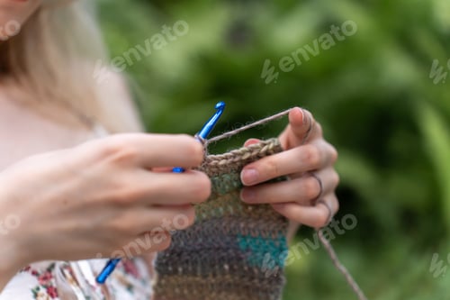Preview: Close-up of female hands crocheting against a nature background