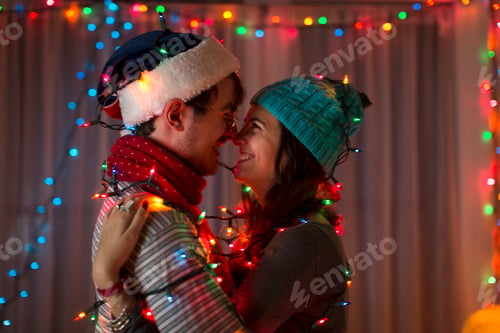 Preview: Romantic young couple wrapped in decorative lights at christmas
