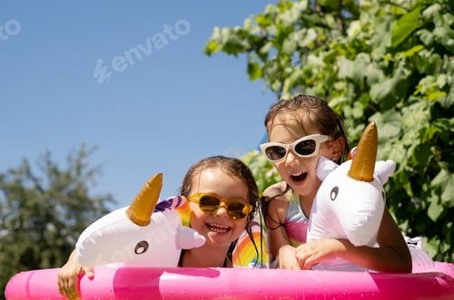 Preview: Two little wet girls in sunglasses are having fun in an inflatable pool
