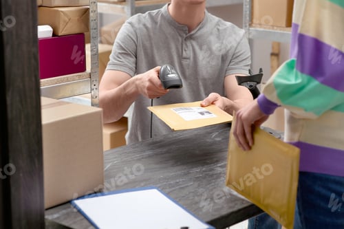 Preview: Woman and post office worker with scanner reading parcel barcode at counter indoors, closeup