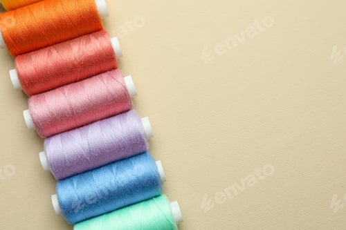 Preview: Set of colorful sewing threads on beige background, flat lay. Space for text