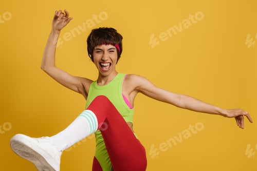 Preview: Excited fit woman in retro styled sports clothing dancing against yellow background