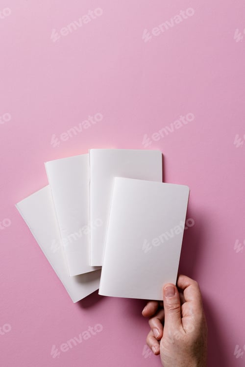Preview: Hand of caucasian woman holding a notebook over other notebooks with copy space on pink background