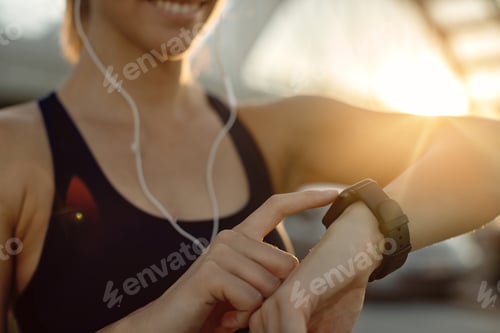 Preview: Close-up of athletic woman using fitness tracker at sunset.