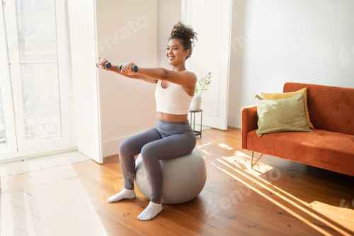 Preview: woman having workout holding dumbbells sitting on stability ball indoors