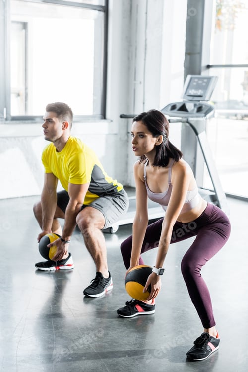 Preview: sportsman and sportswoman doing squat with balls in sports center