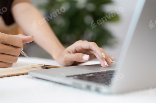 Preview: Close-up of Hands Typing on Laptop and Writing in Notebook in Modern Workspace