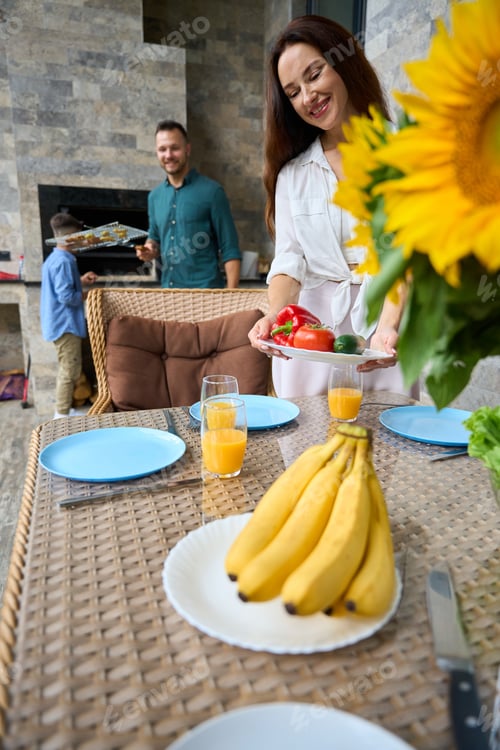 Preview: Happy woman setting the table on the terrace