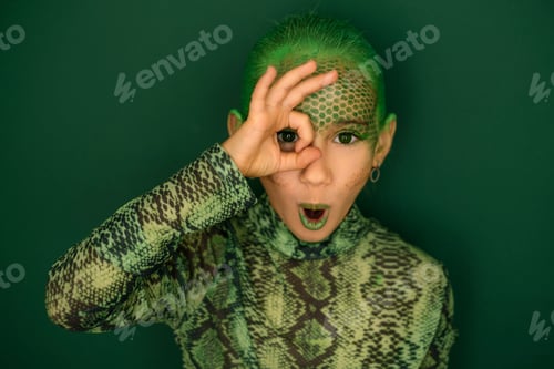 Preview: A girl disguised as a snake shows an ok gesture, covering her eye with her hand.