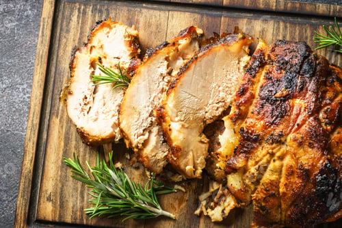 Preview: Roasted pork with herbs on wooden cutting board.